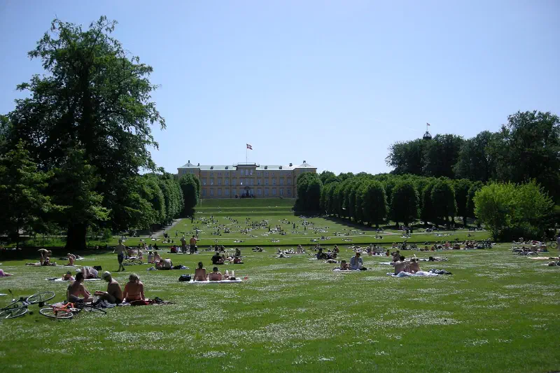 Folk på plænen i Frederiksberg Have, med Frederiksberg Slot øverst på skråningen.