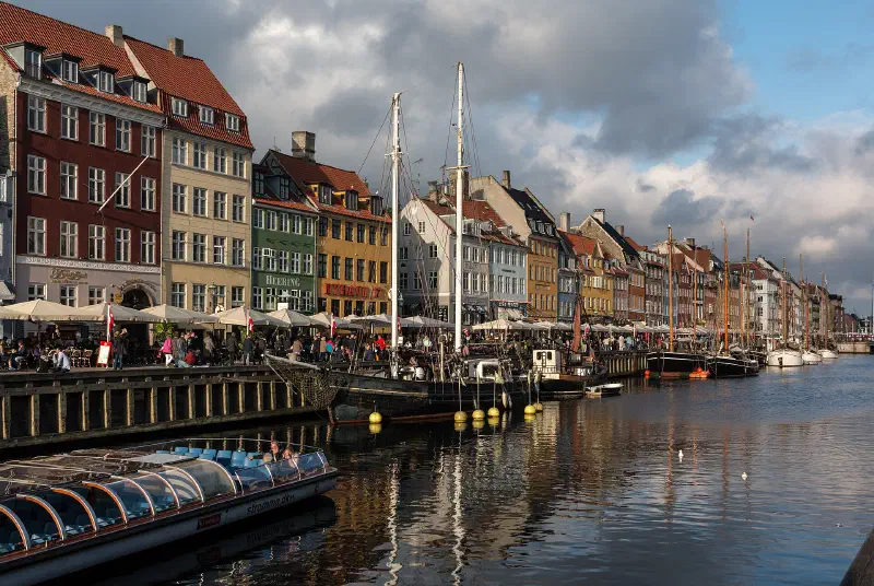 Aften ved Nyhavn: caféparasoller og gæster langs kanalen, med fortøjede træskibe.
