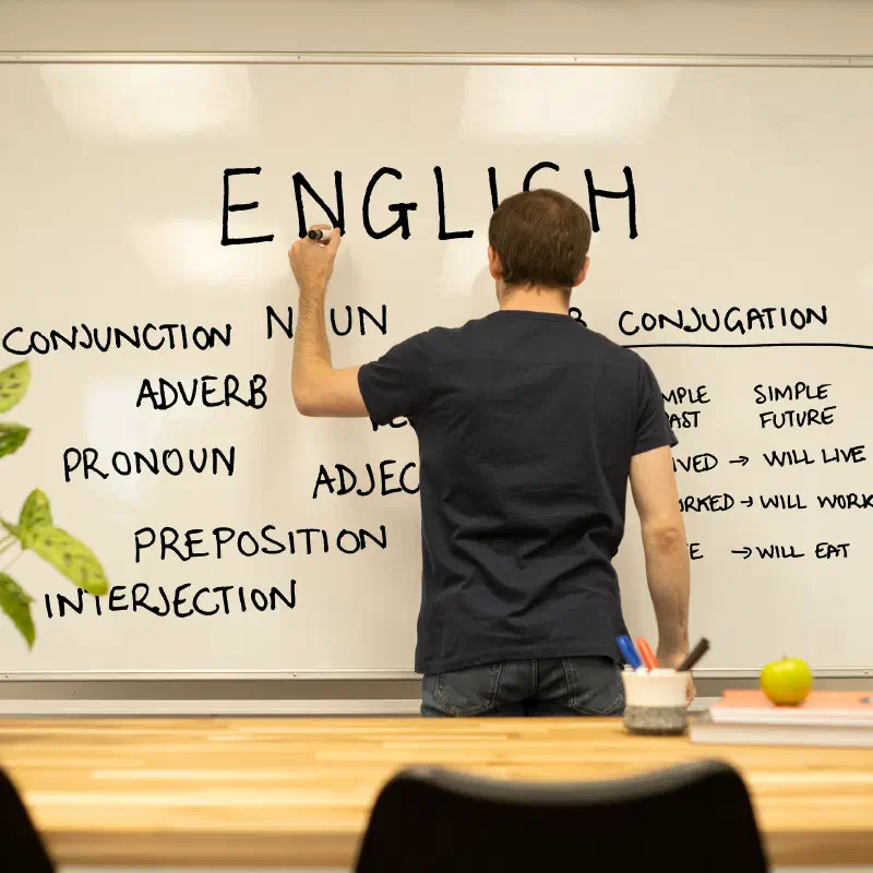 A teacher writing an English lesson on a whiteboard.